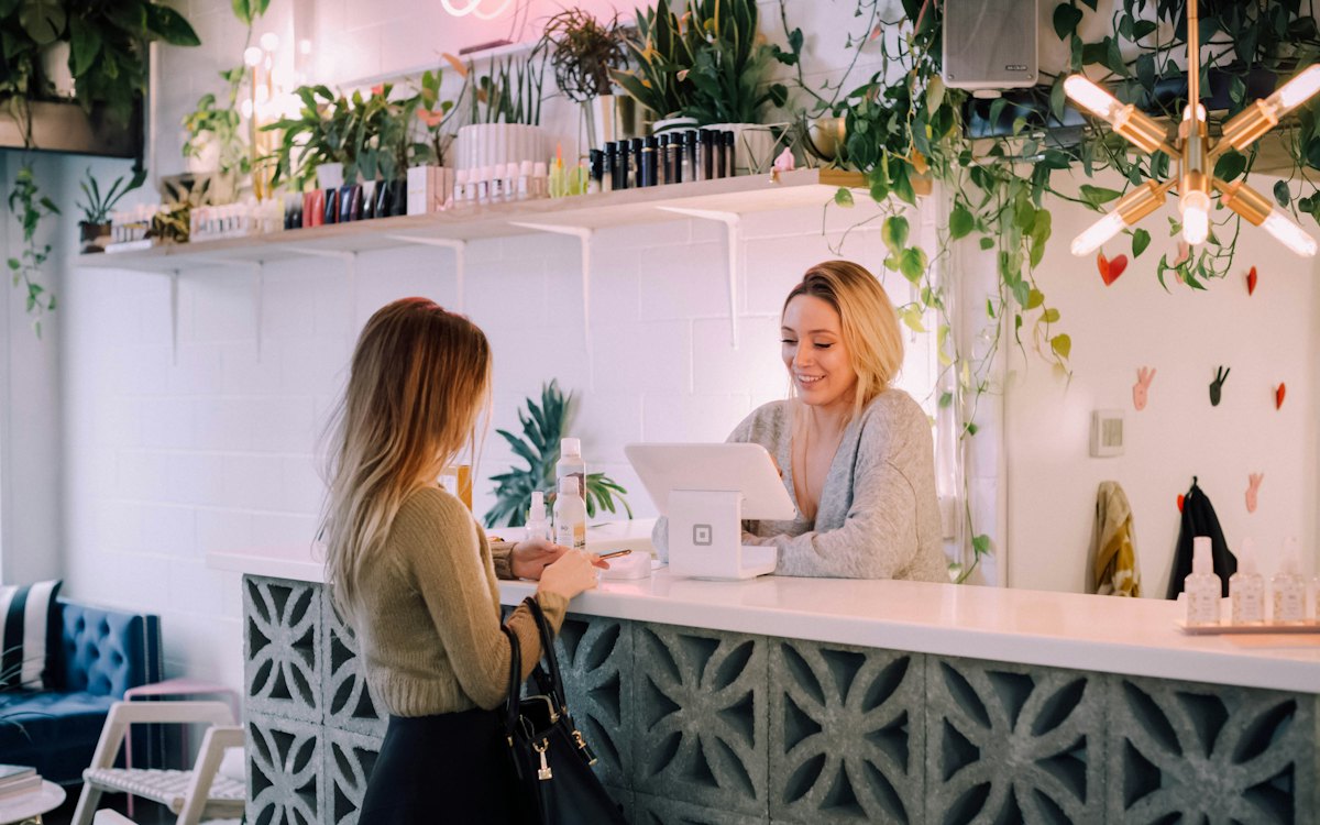 A customer paying at the counter of a plant-filled shop while a clerk smiles